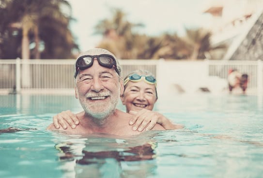 Ein altes Paar steht im Pool und lacht in die Kamera, weil es per Express rechtzeitig die Schwimmbrillen erhalten hat